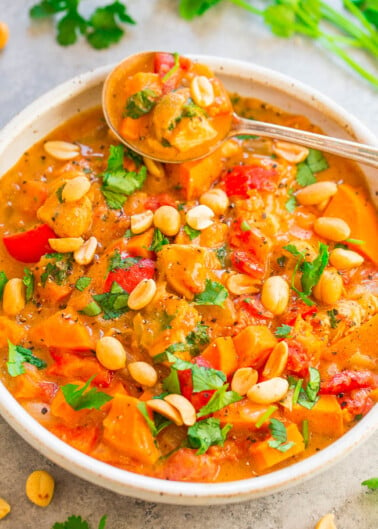 A bowl of hearty vegetable stew with chickpeas, tomatoes, and carrots, garnished with fresh herbs and peanuts.