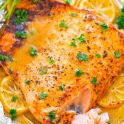 Oven-baked salmon fillet seasoned with spices, garnished with parsley and lemon slices.