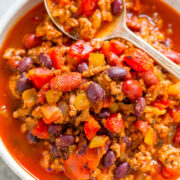 A bowl of chili with ground meat, kidney beans, and diced vegetables, served with a spoon.
