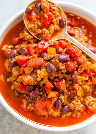 A bowl of chili with ground meat, kidney beans, and diced vegetables, served with a spoon.