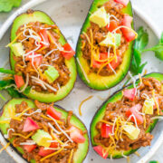 Stuffed avocado halves with taco filling and shredded cheese, garnished with diced tomato.