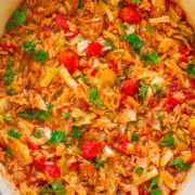 A pot of tomato-based stew with ground meat, chopped vegetables, and garnished with fresh herbs.