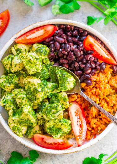 A colorful bowl of rice, black beans, pesto chicken, and fresh tomatoes garnished with cilantro.