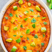A baked casserole topped with melted cheese, diced avocado, and cilantro in a white baking dish.
