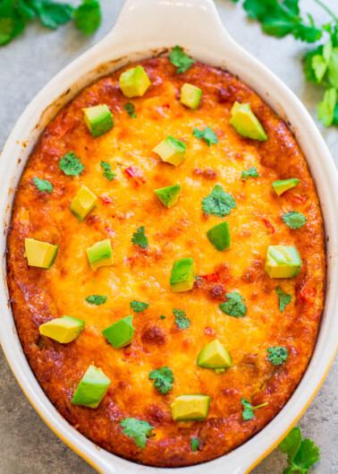 A baked casserole topped with melted cheese, diced avocado, and cilantro in a white baking dish.