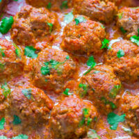 Baked meatballs in tomato sauce garnished with fresh cilantro.