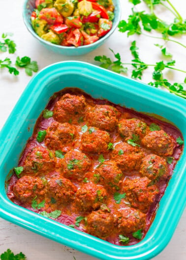 Baked meatballs garnished with fresh herbs in a blue casserole dish.