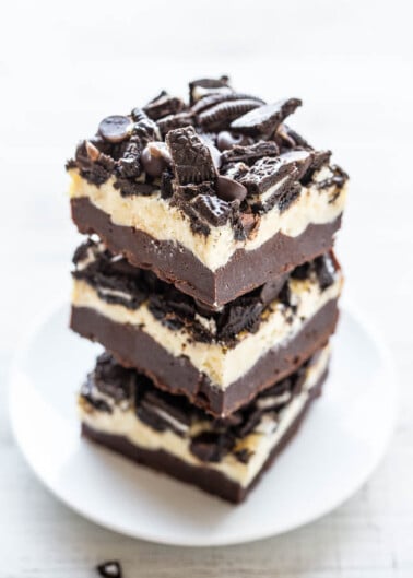 A stack of oreo cheesecake bars garnished with cookie pieces on a white plate.