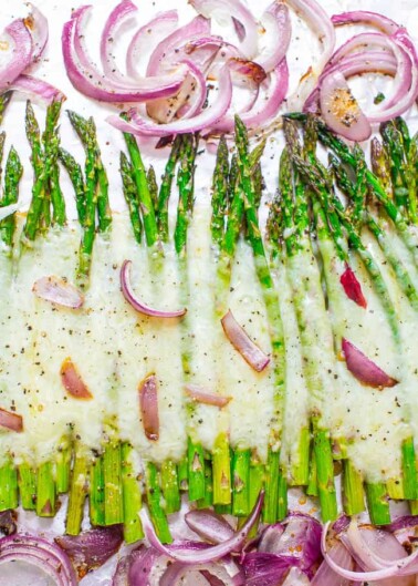 Baked asparagus with melted cheese and red onion slices on a baking sheet.