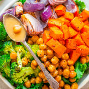 A bowl filled with roasted vegetables and chickpeas, with a spoon drizzling sauce over the top.