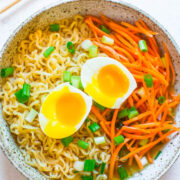 A bowl of ramen noodles with soft-boiled egg, sliced carrots, and chopped green onions.