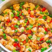 A colorful chicken stir-fry dish with black beans, corn, red bell peppers, and garnished with chopped spring onions and cilantro.