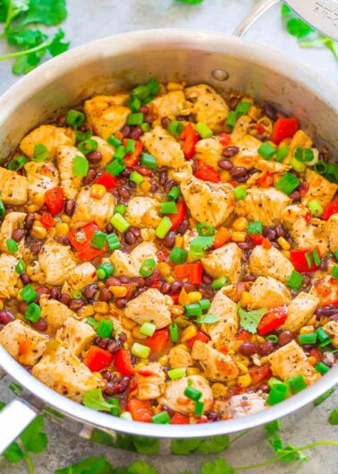 A colorful chicken stir-fry dish with black beans, corn, red bell peppers, and garnished with chopped spring onions and cilantro.