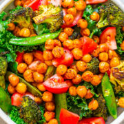 A colorful salad bowl containing roasted chickpeas, broccoli, snap peas, tomatoes, and kale.