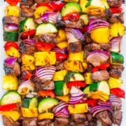 Colorful grilled vegetable and beef kabobs on a white plate.