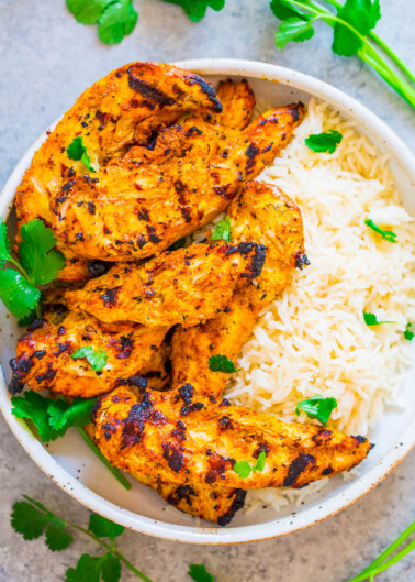 Grilled chicken with herbs served alongside white rice in a bowl.