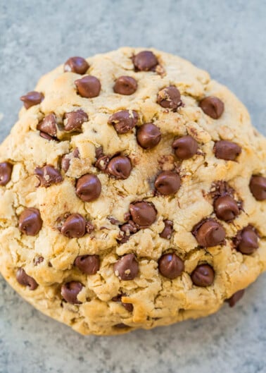 A large chocolate chip cookie on a gray surface.