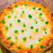 Baked cheese dip garnished with green onions, served with chips and celery sticks.