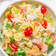 A bowl of pasta salad with tomatoes, greens, and ham.