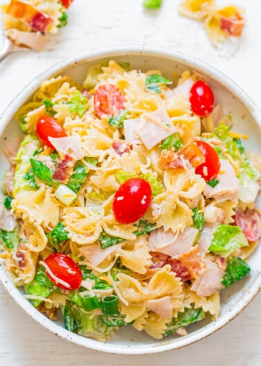 A bowl of pasta salad with tomatoes, greens, and ham.