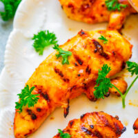 Grilled chicken breasts garnished with parsley on a white plate.