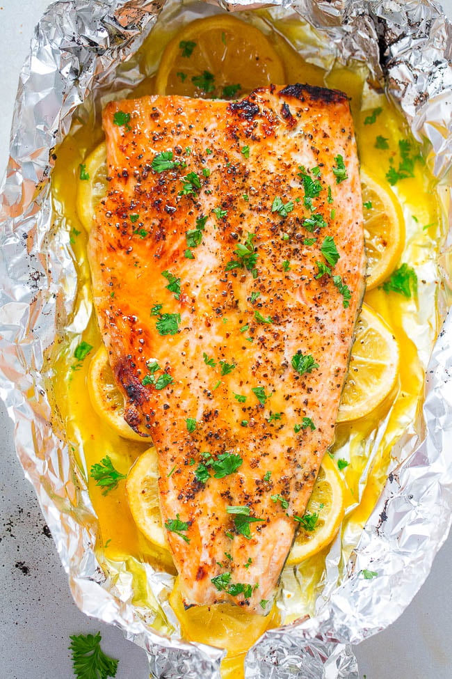 Baked salmon fillet seasoned with herbs and pepper, placed on lemon slices in a foil packet, garnished with fresh parsley.