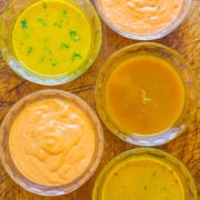 Assorted dressings or sauces in transparent bowls on a wooden surface.