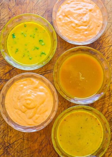 Assorted dressings or sauces in transparent bowls on a wooden surface.