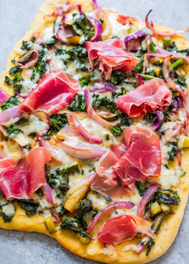 A freshly baked pizza topped with cheese, cured meats, and vegetables on a stone countertop.