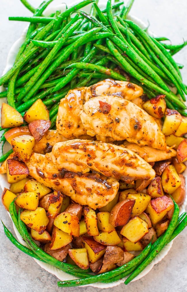 A plate with glazed chicken tenders, roasted potato cubes, and sautรฉed green beans arranged in separate sections.