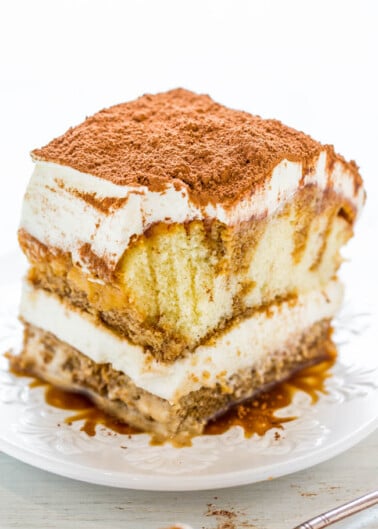 A slice of tiramisu with distinct layers of mascarpone cream and soaked sponge cake, dusted with cocoa powder, on a white plate.