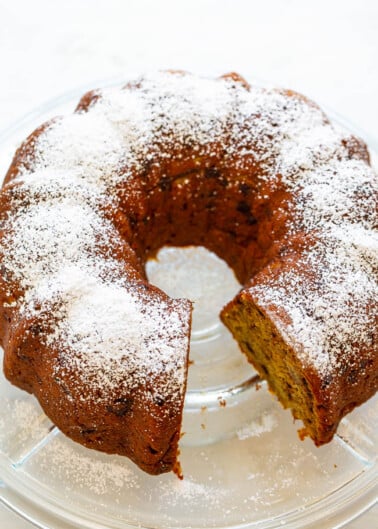 A bundt cake with a dusting of powdered sugar on a glass serving plate.