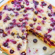 A freshly baked blueberry cake in a glass dish, with whole blueberries scattered around.