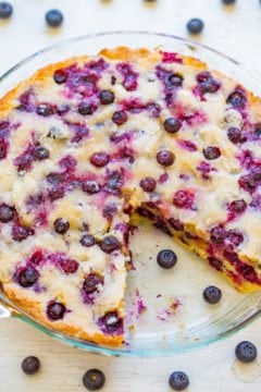 A freshly baked blueberry cake in a glass dish, with whole blueberries scattered around.