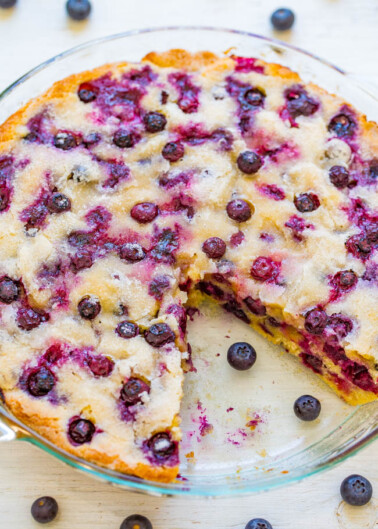 A freshly baked blueberry cake in a glass dish, with whole blueberries scattered around.