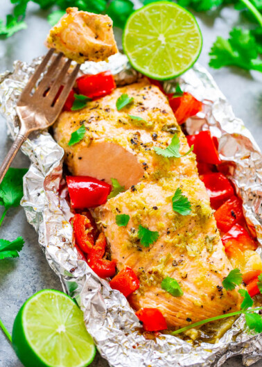 Grilled salmon fillet with lime and diced red peppers, served in foil with a fork on the side.