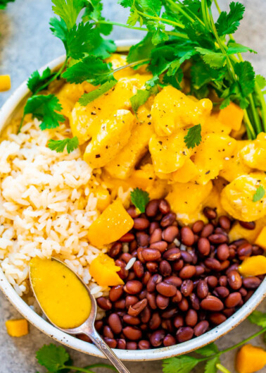 A colorful bowl of rice, beans, and curry with a garnish of fresh herbs.