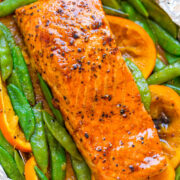 Grilled salmon fillet with snap peas and sliced carrots on aluminum foil.