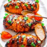 Grilled chicken breasts with a glazed coating, garnished with fresh herbs on a white plate.