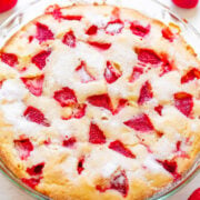 Freshly baked strawberry cake in a glass dish, surrounded by whole strawberries.