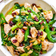 A colorful stir-fry dish with chicken, broccoli, snap peas, and cranberries in a white bowl.