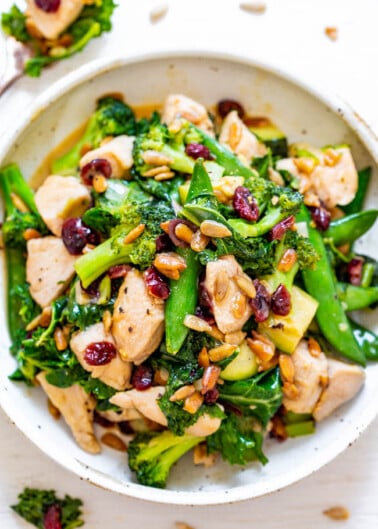 A colorful stir-fry dish with chicken, broccoli, snap peas, and cranberries in a white bowl.