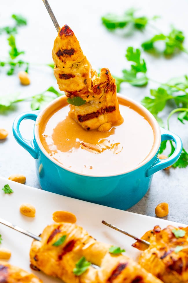 Grilled chicken skewer dipped into a creamy peanut sauce, garnished with chopped herbs.