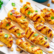 Grilled chicken skewers garnished with cilantro and peanuts on a white platter.