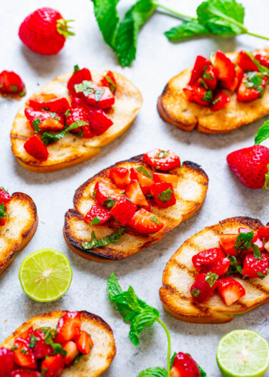 Slices of toasted bread topped with fresh diced strawberries, lime, and mint leaves.