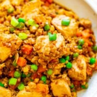 A bowl of chicken fried rice with peas, carrots, and green onions.