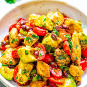 A colorful bowl of chicken salad with avocados, cherry tomatoes, beans, and herbs.