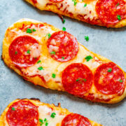 Three pepperoni flatbread pizzas garnished with parsley on a light grey surface.