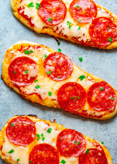 Three pepperoni flatbread pizzas garnished with parsley on a light grey surface.