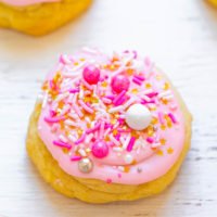 A freshly baked cookie topped with pink icing and colorful sprinkles.